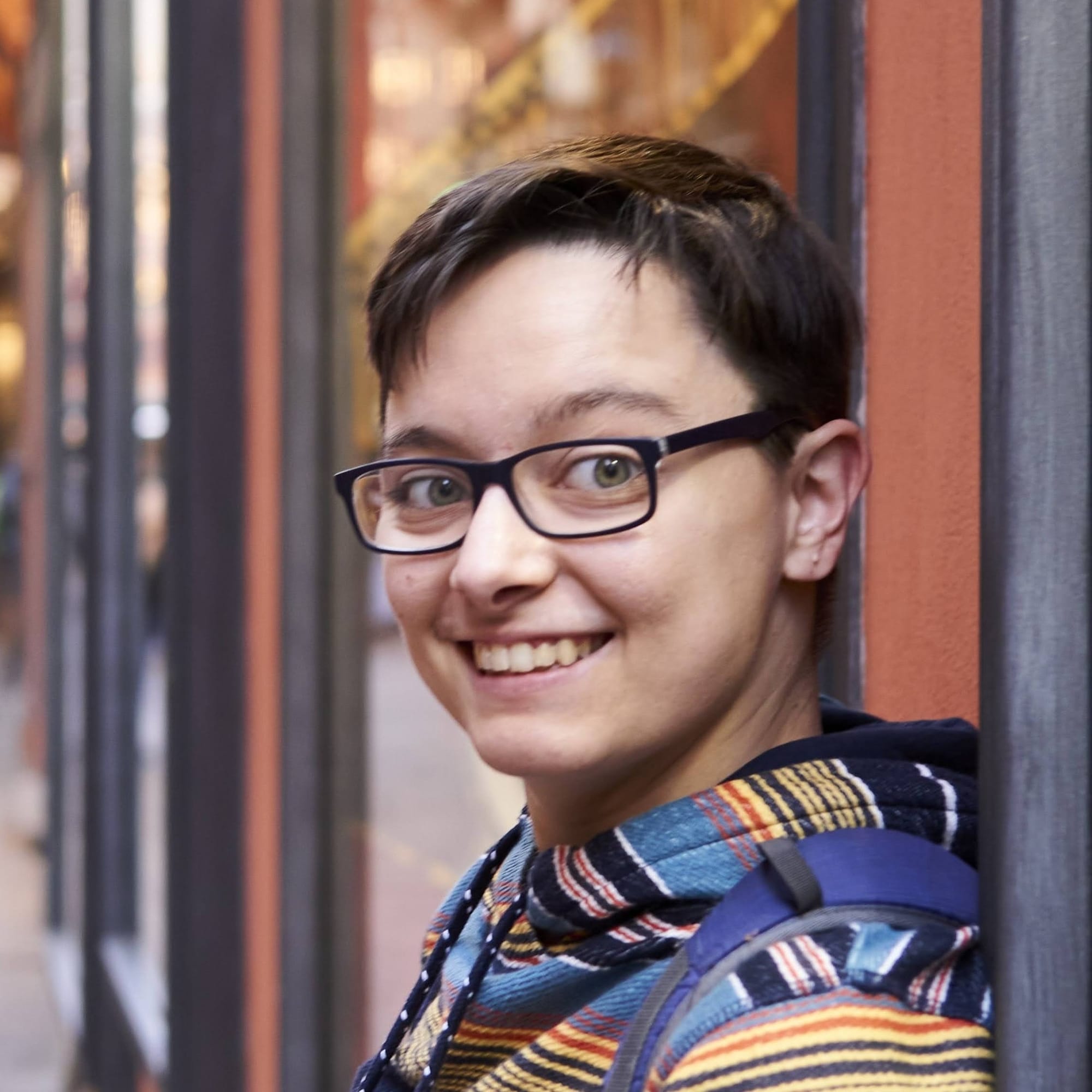Finley smiles at the camara. They have a light skin tone, glasses, short brown hair and are wearing a blue and yellow striped hoodie.